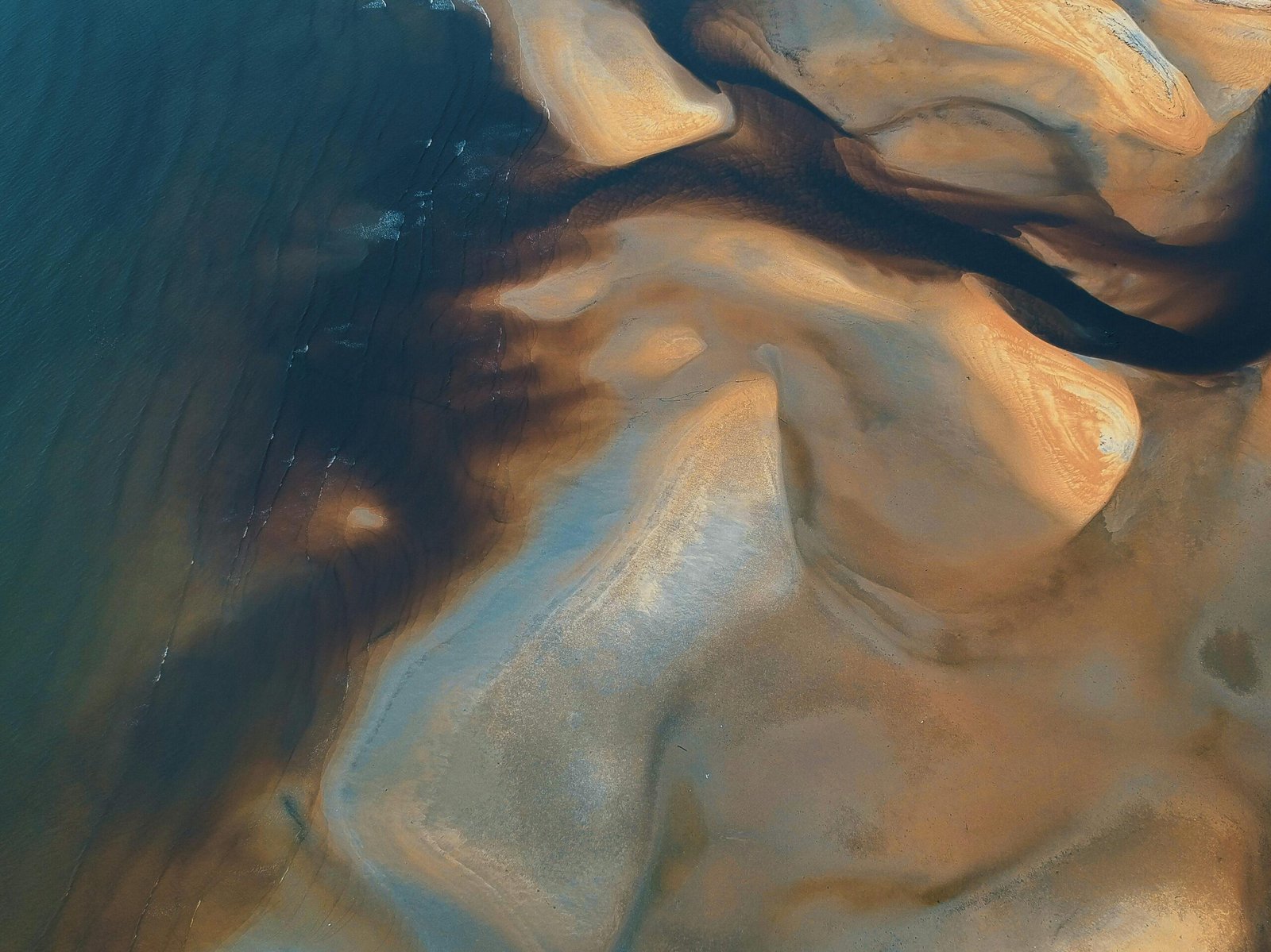 Aerial photograph capturing intricate sand and water patterns on a Malaysian coast.